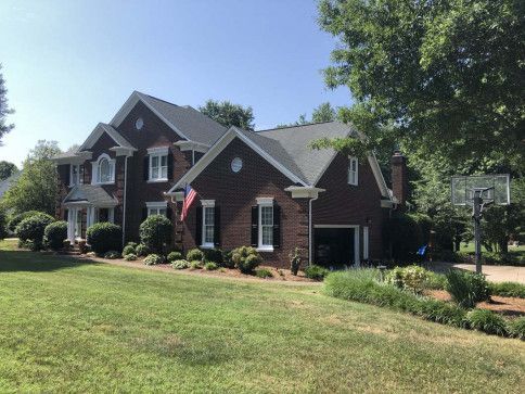 Brick house with black roof, white trim, and American flag on the front. Garage and basketball hoop visible.
