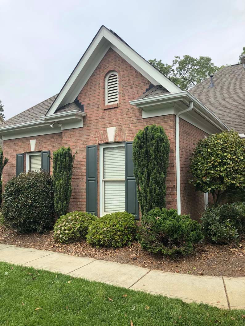 Brick house with shutters and landscaping, under a cloudy sky.