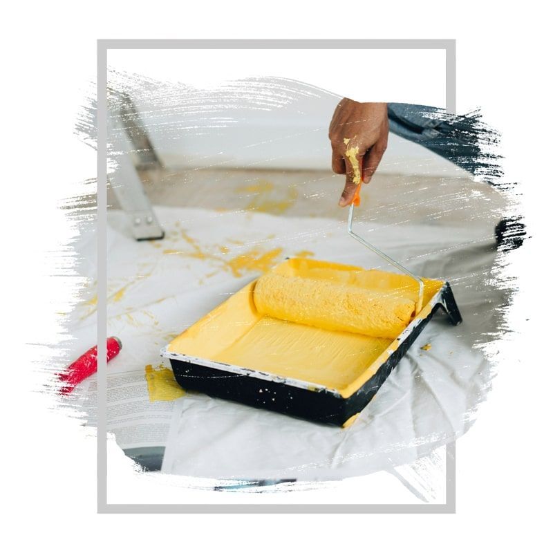 A person painting with yellow paint using a roller and paint tray.