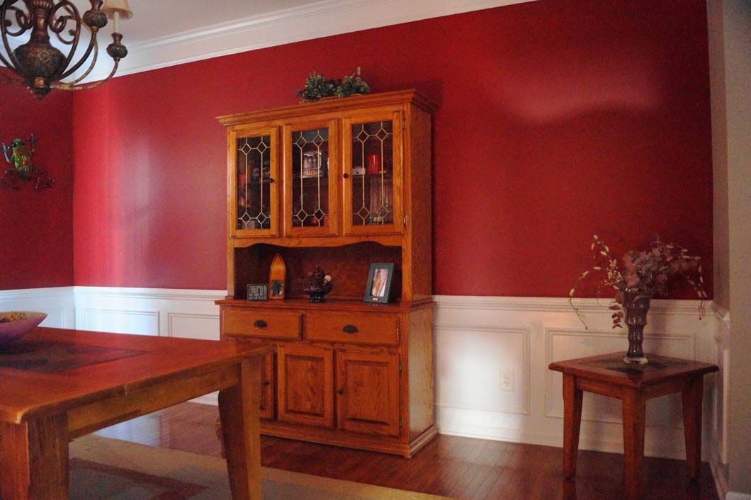 Dining room with red walls, white wainscoting, and a wooden hutch.