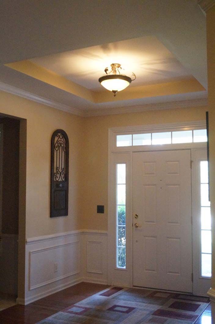 Entryway with white door, light fixture, beige walls, and wood floor.