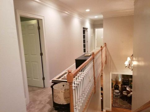 Hallway with stairs and multiple doorways, lit with overhead lights. Cream-colored walls, white trim.