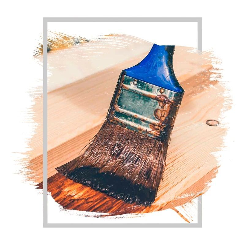 Brush applying dark stain to a wooden surface.