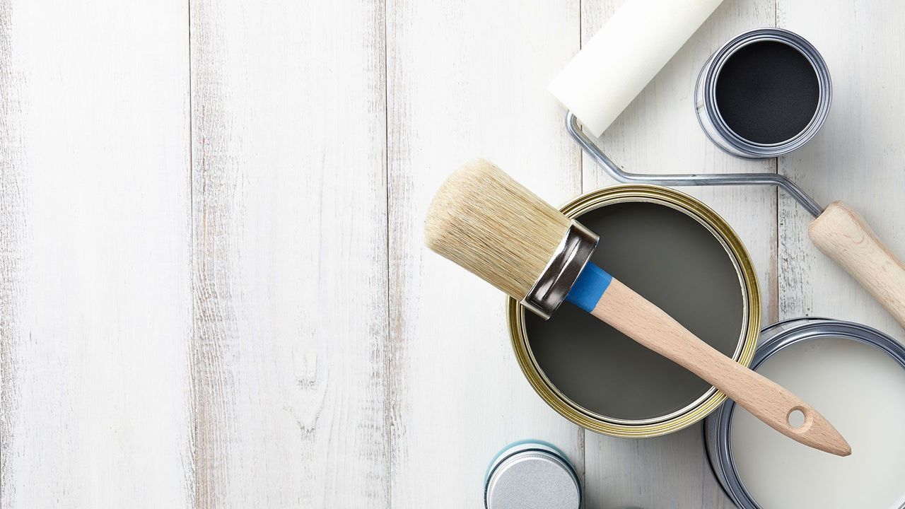 Paint cans, brushes, and rollers on a white wooden surface, ready for painting.