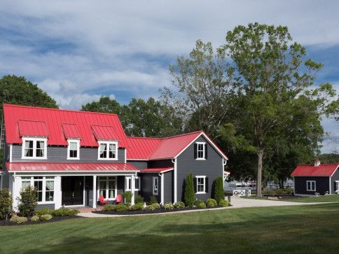 Gray house with red metal roof, white trim, and a small outbuilding, on a green lawn under a blue sky.