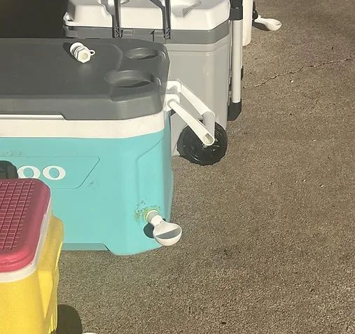 Coolers with wheels and drain spouts on pavement, including a turquoise, gray, and yellow cooler.
