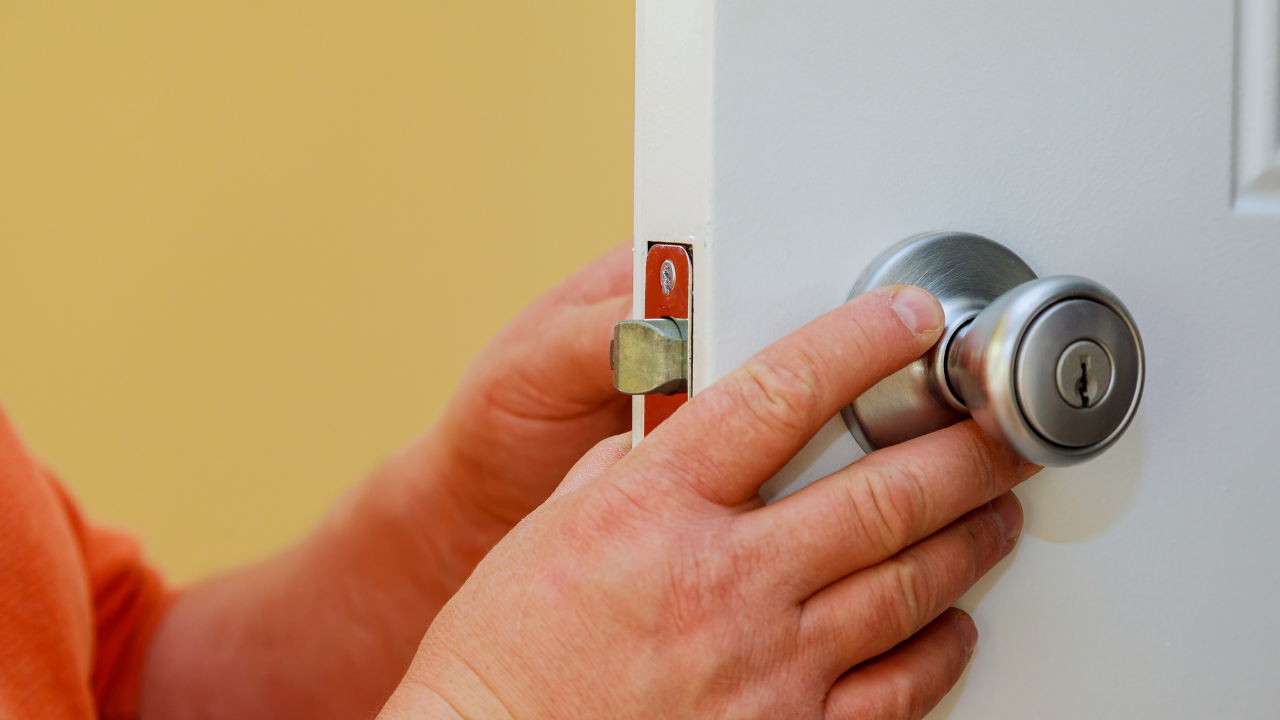 Hand turning a silver doorknob on a white door, with a yellow wall in the background