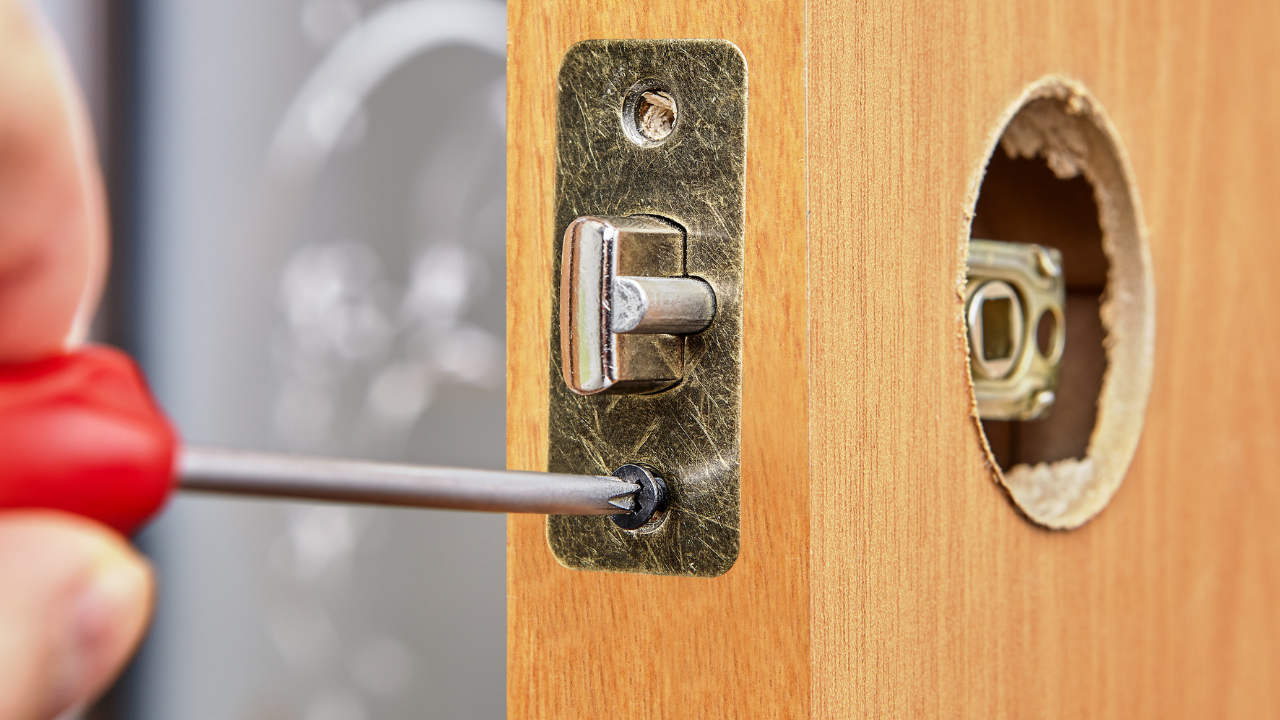 Screwdriver removing a door lock latch from a wooden door edge