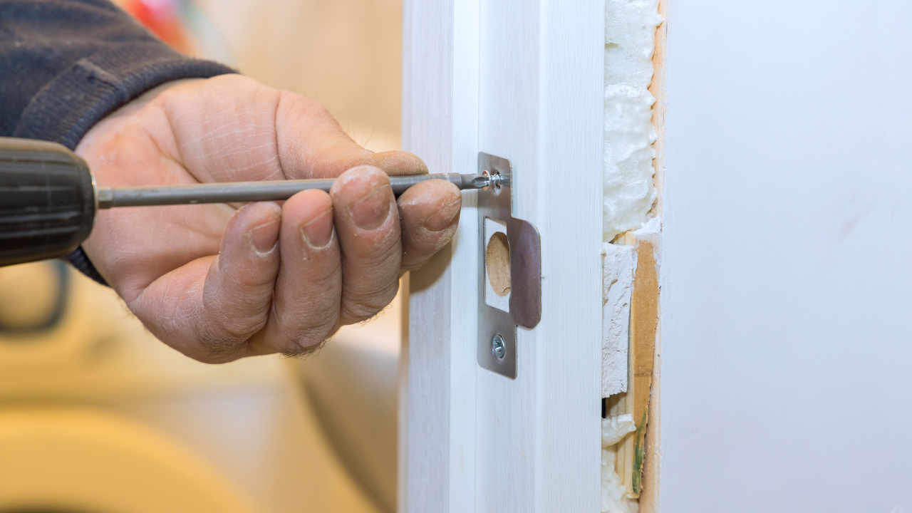 Hand using a screwdriver to adjust a door latch on a white door frame