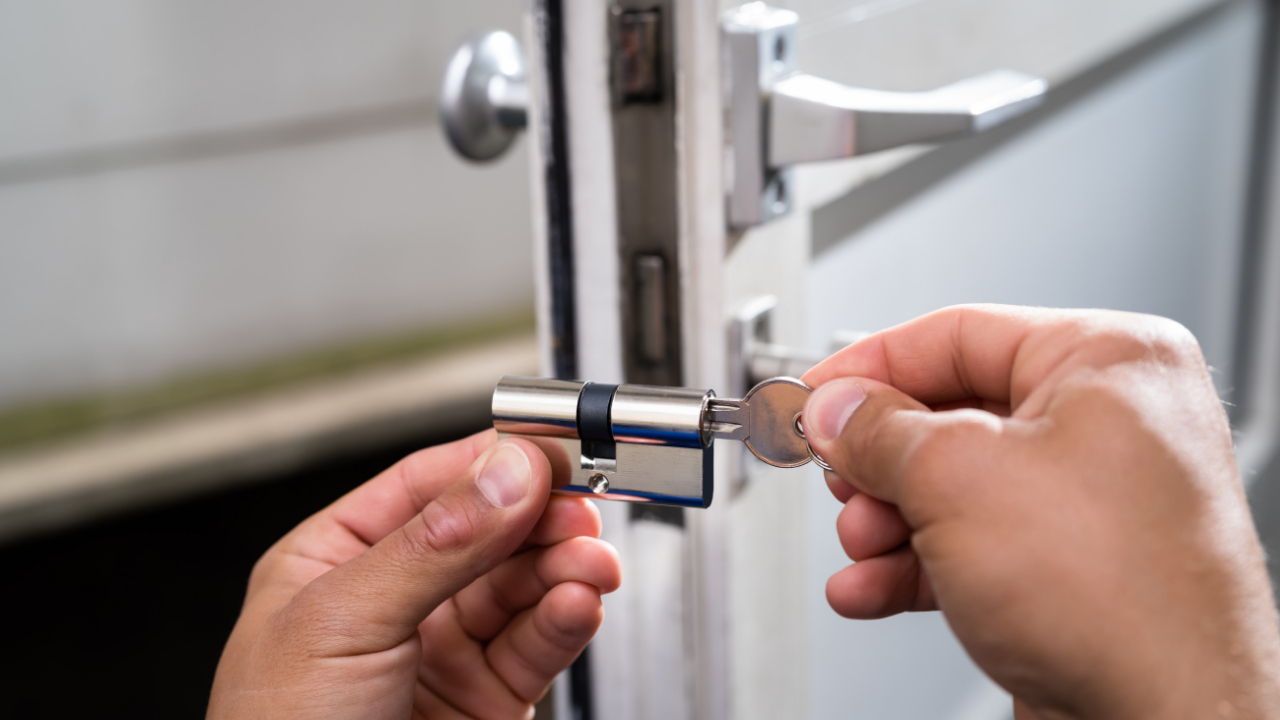 Hands using a wrench to tighten a silver door lock on a white door