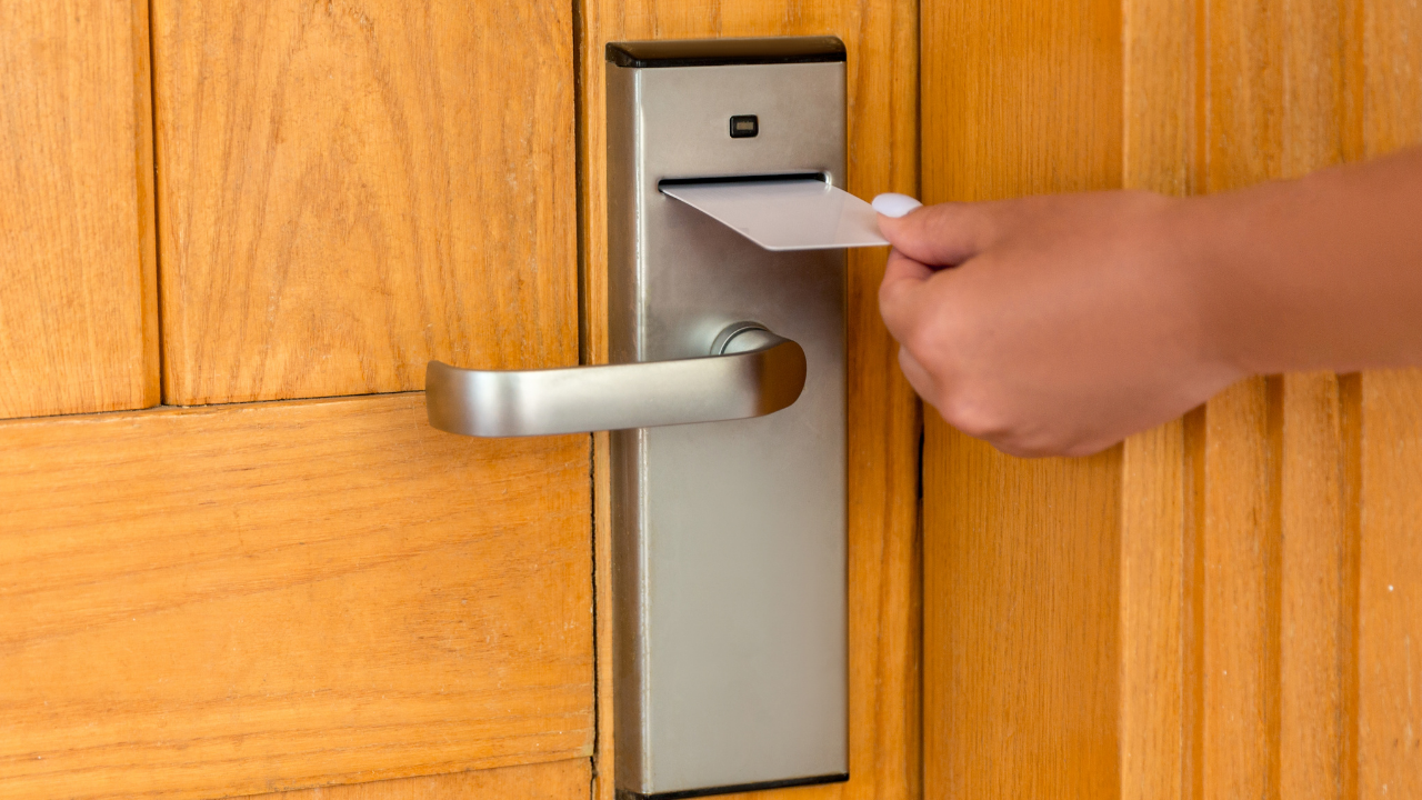 Hand inserting a key card into a silver hotel room door lock on a wooden door