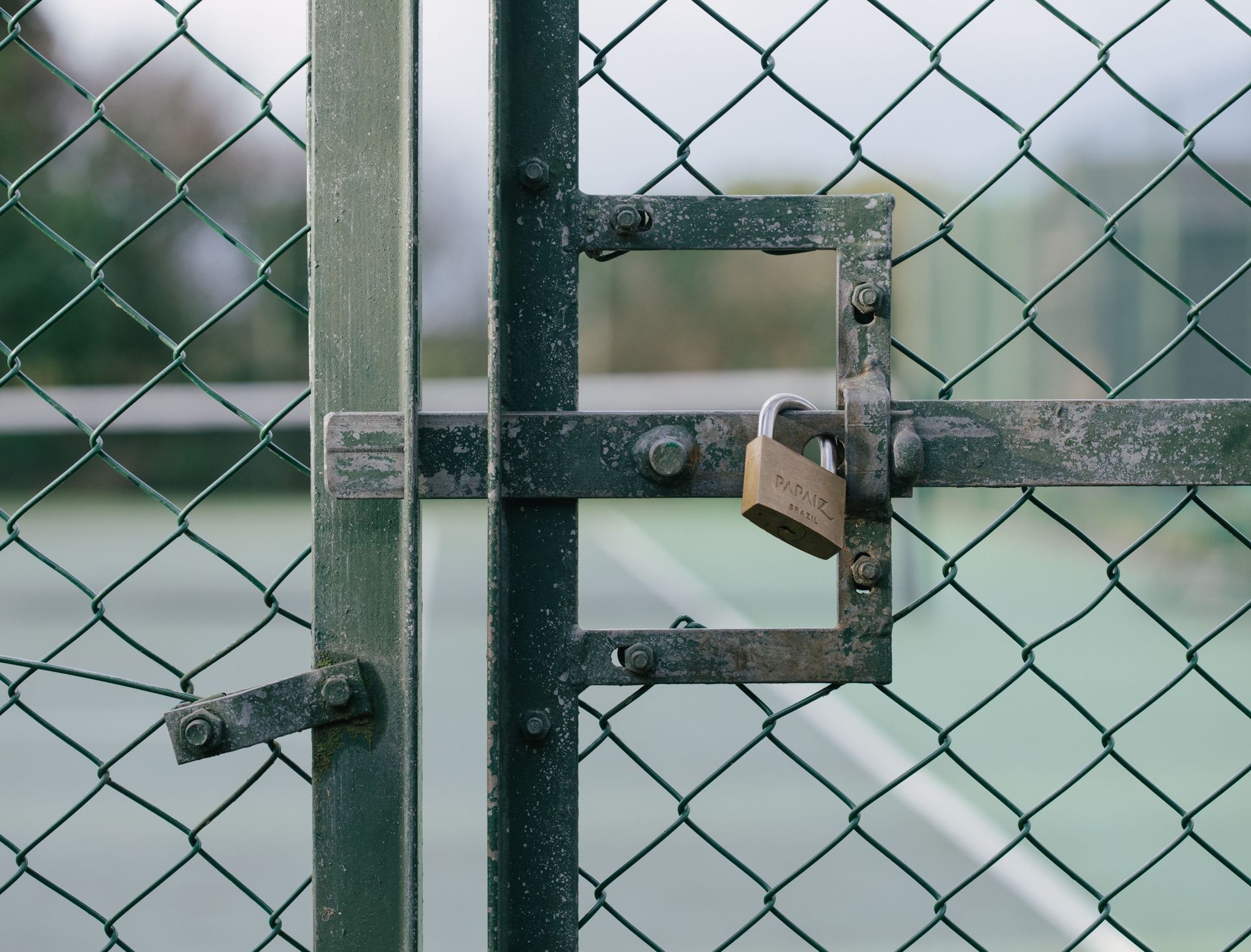 Padlocked chain-link gate on a wet tennis court