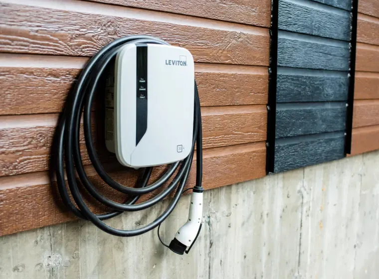 White electric car charger mounted on an exterior wall with coiled black cable.