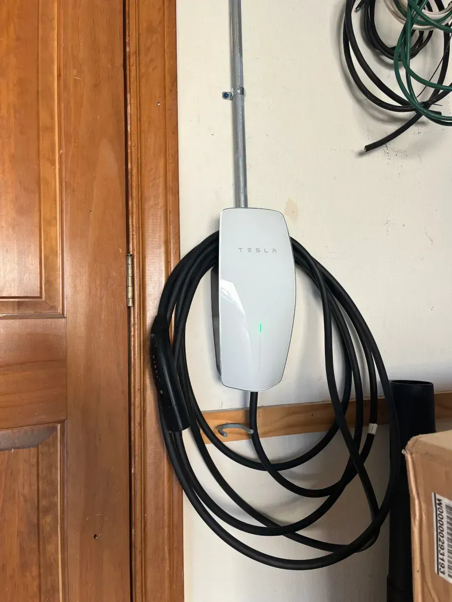 White wall-mounted device with coiled black cables beside a wooden door in a utility area