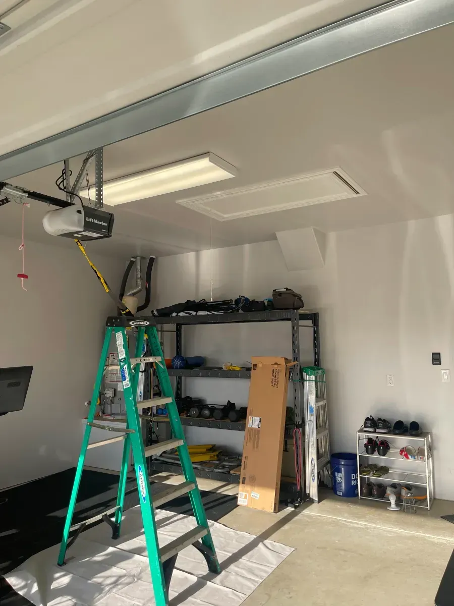 Green ladder in a garage under a ceiling-mounted opener, with shelving and tools along the wall.
