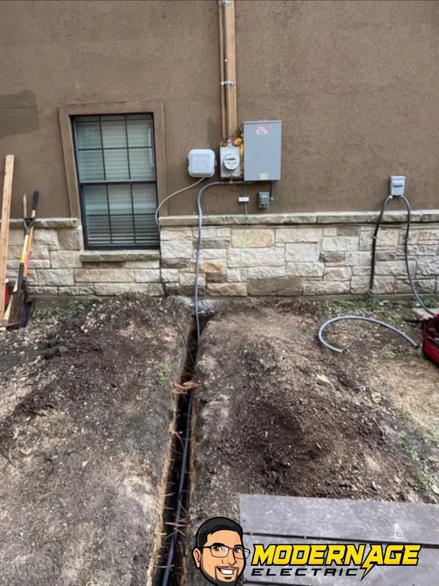 Residential basement wall with exposed foundation trench, utility boxes, and a window above stone veneer.
