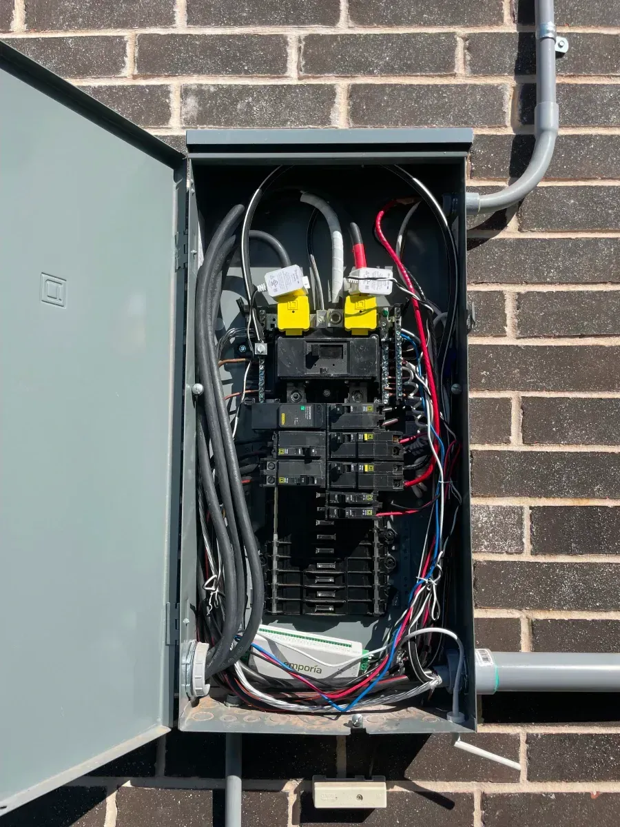 Open electrical panel on a brick wall with wires and circuit breakers visible