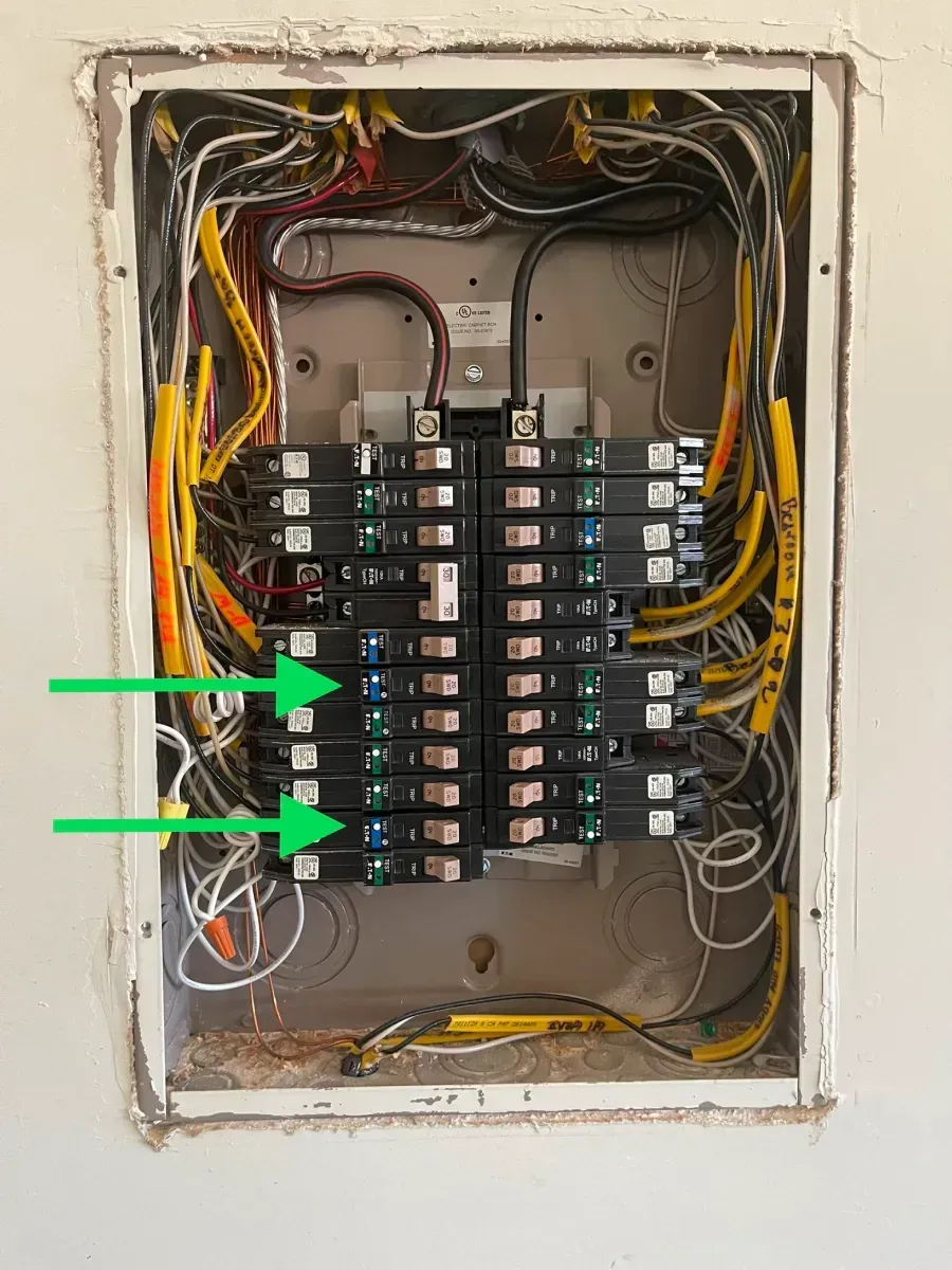 Open electrical breaker panel with two green arrows pointing to lower left breakers