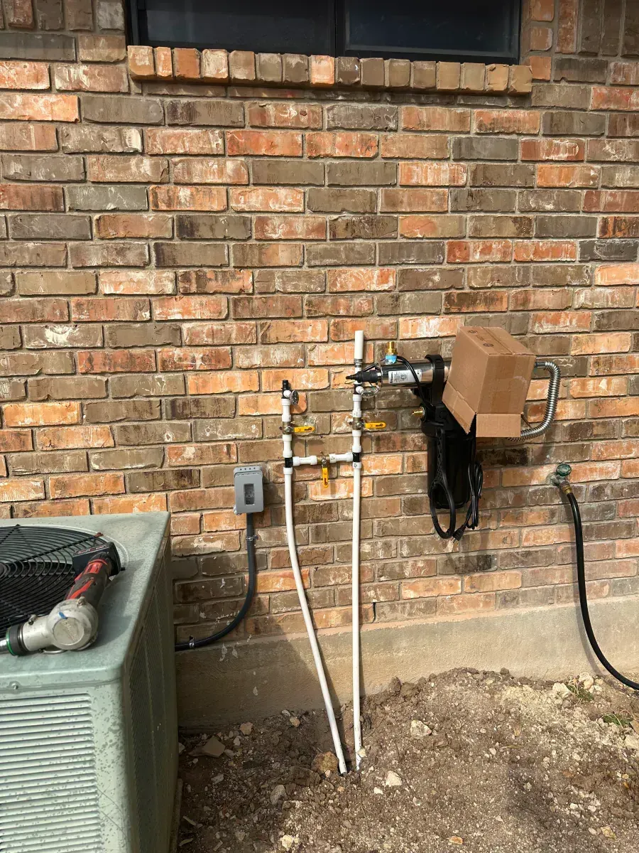 Outdoor brick wall with utility pipes, valves, and a small meter box beside an HVAC unit