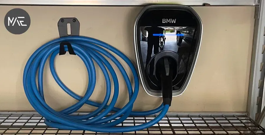 Blue coiled cable hanging beside a black BMW EV charger on a wall-mounted rack
