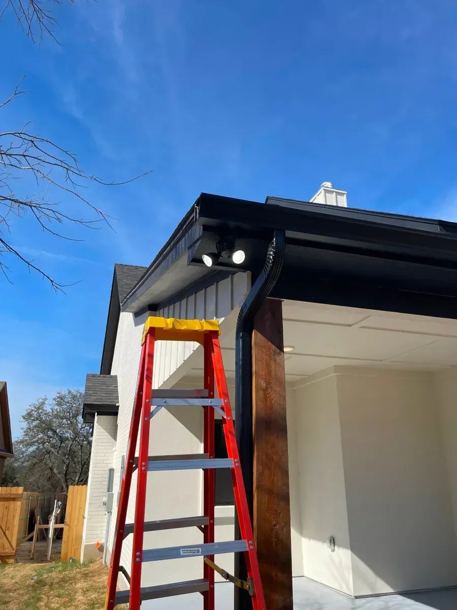 Red ladder leaning against a house roof under bright blue sky