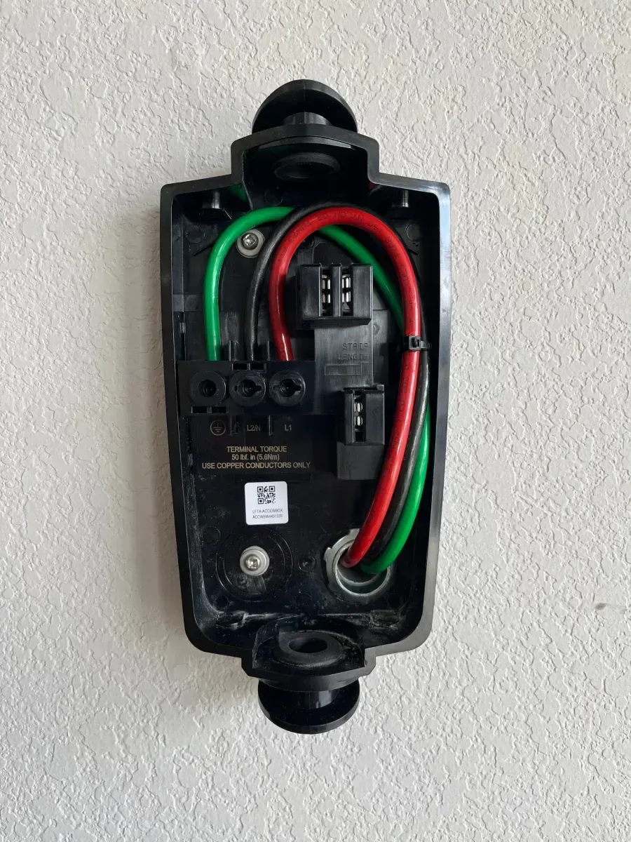 Open electrical junction box with red, green, and black wires mounted on a wall.