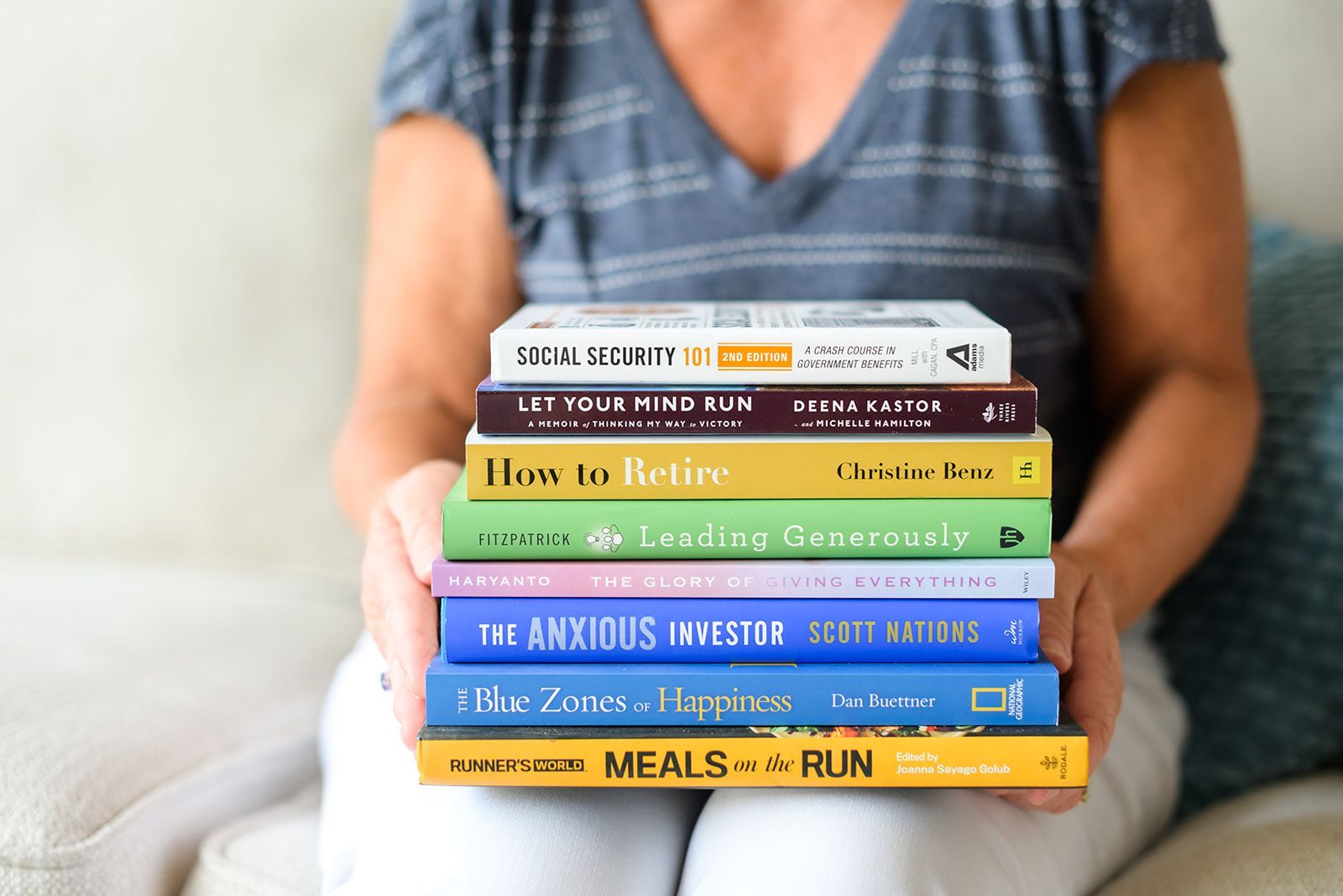 Stack of colorful books held in front of a person seated indoors