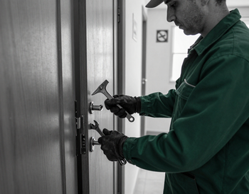 Técnico con uniforme verde instalando una cerradura de puerta con herramientas en un pasillo.
