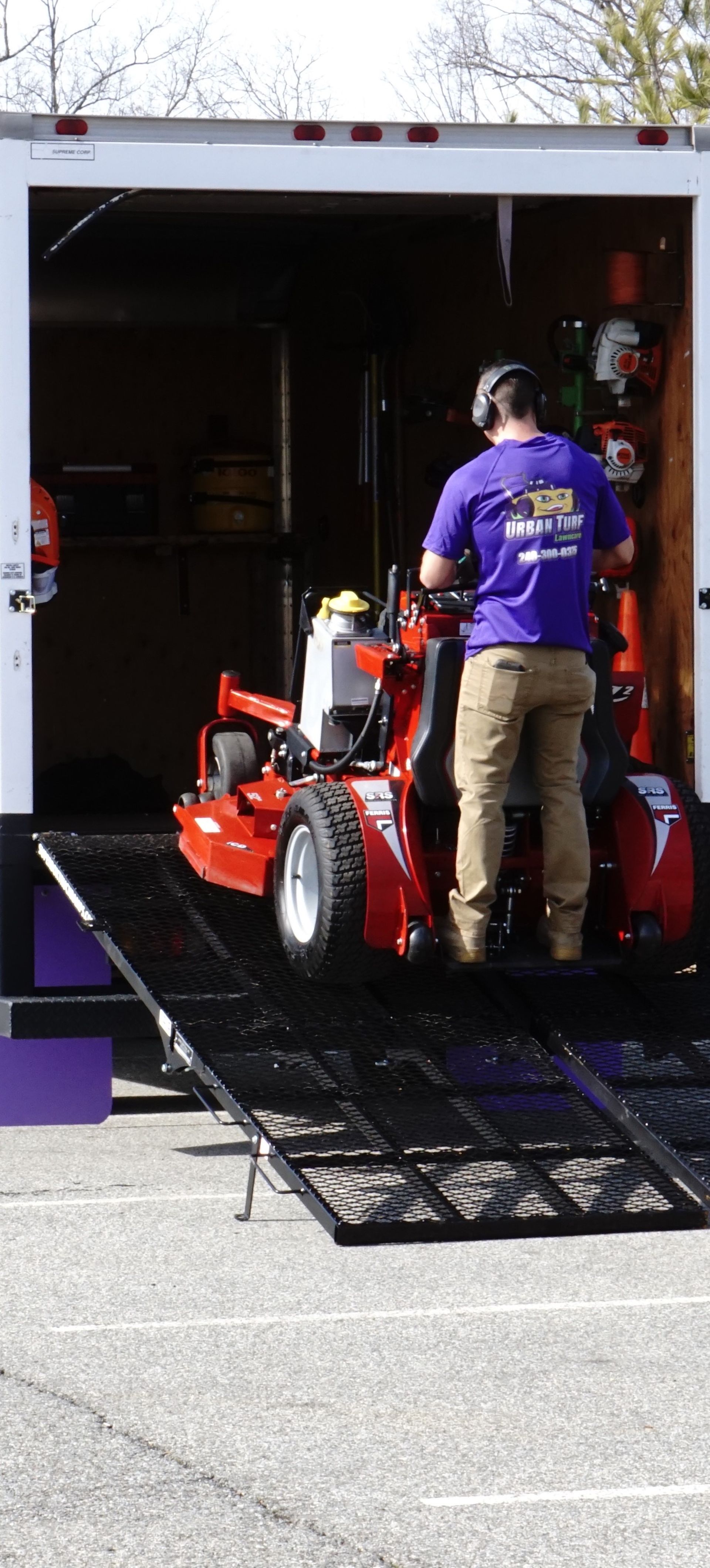 A man is loading a lawn mower into a trailer.