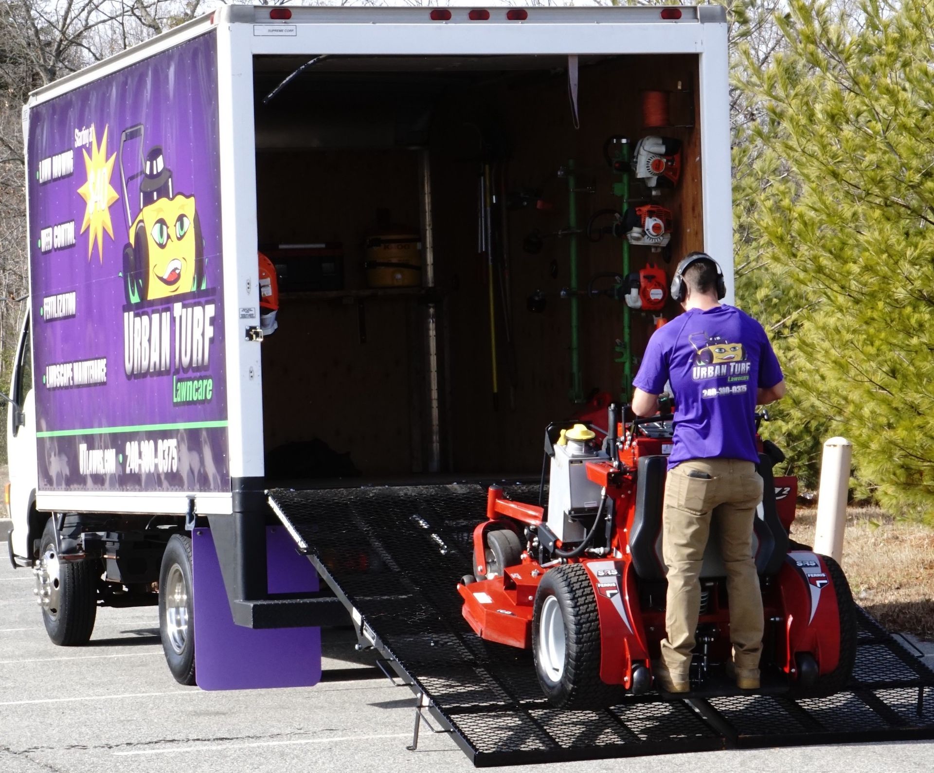 A man is loading a lawn mower into the back of a truck that says cold tuff