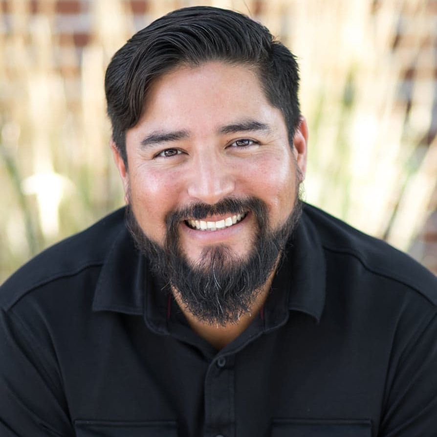 A man with a beard is smiling for the camera while wearing a black shirt.