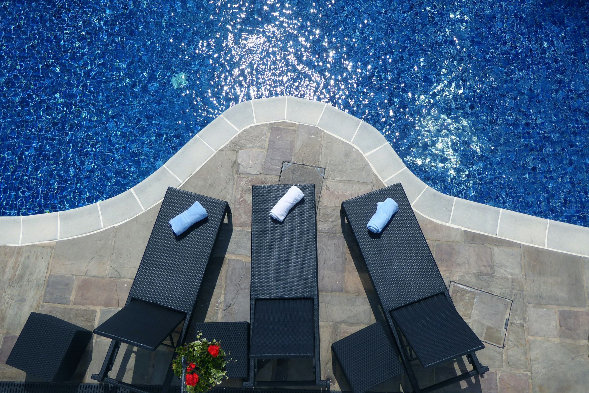 Three lounge chairs with towels next to a pool on a sunny day.