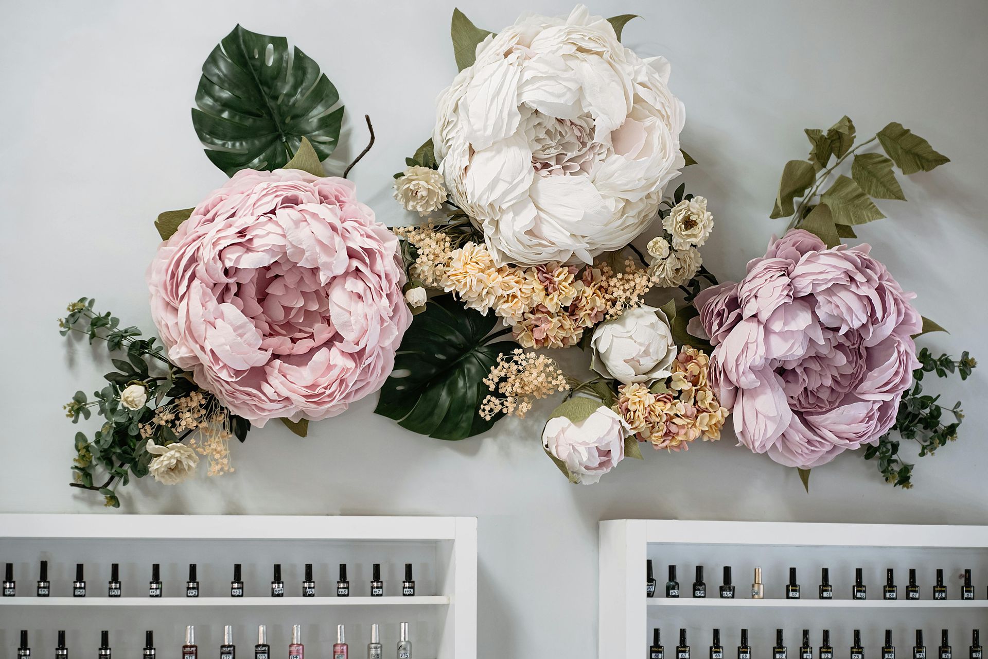 Pink, white, and lavender floral wall arrangement above white shelving in a bright room.