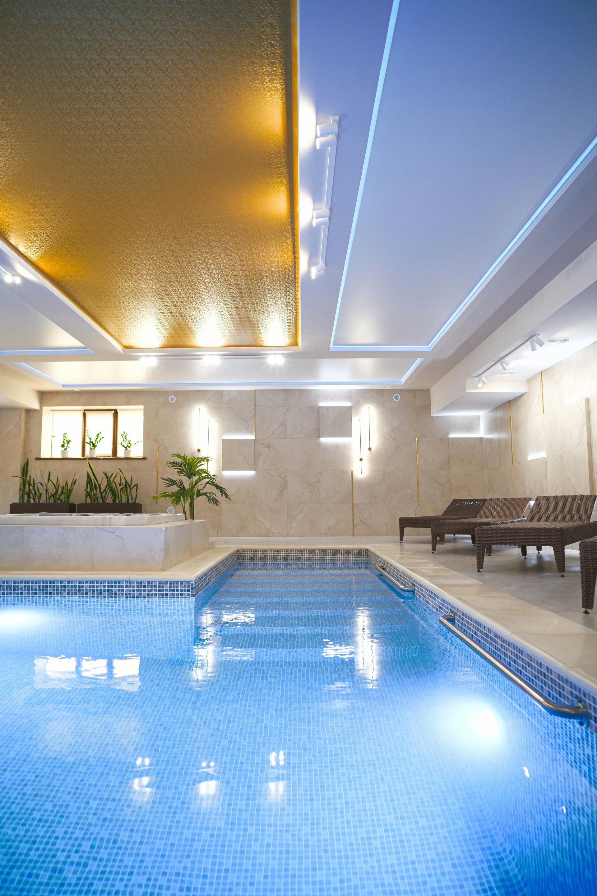 Indoor pool with blue water, warm ceiling lights, and lounge chairs by large windows.