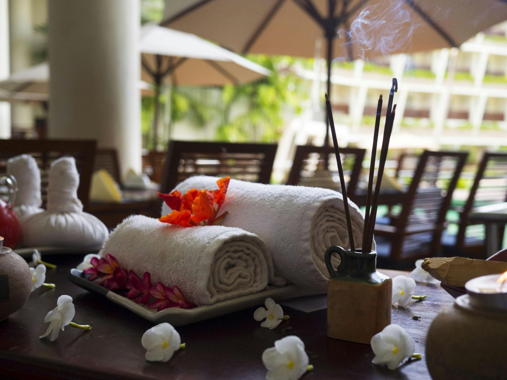 Spa treatment table with rolled white towels, orange flowers, and candles in an outdoor setting