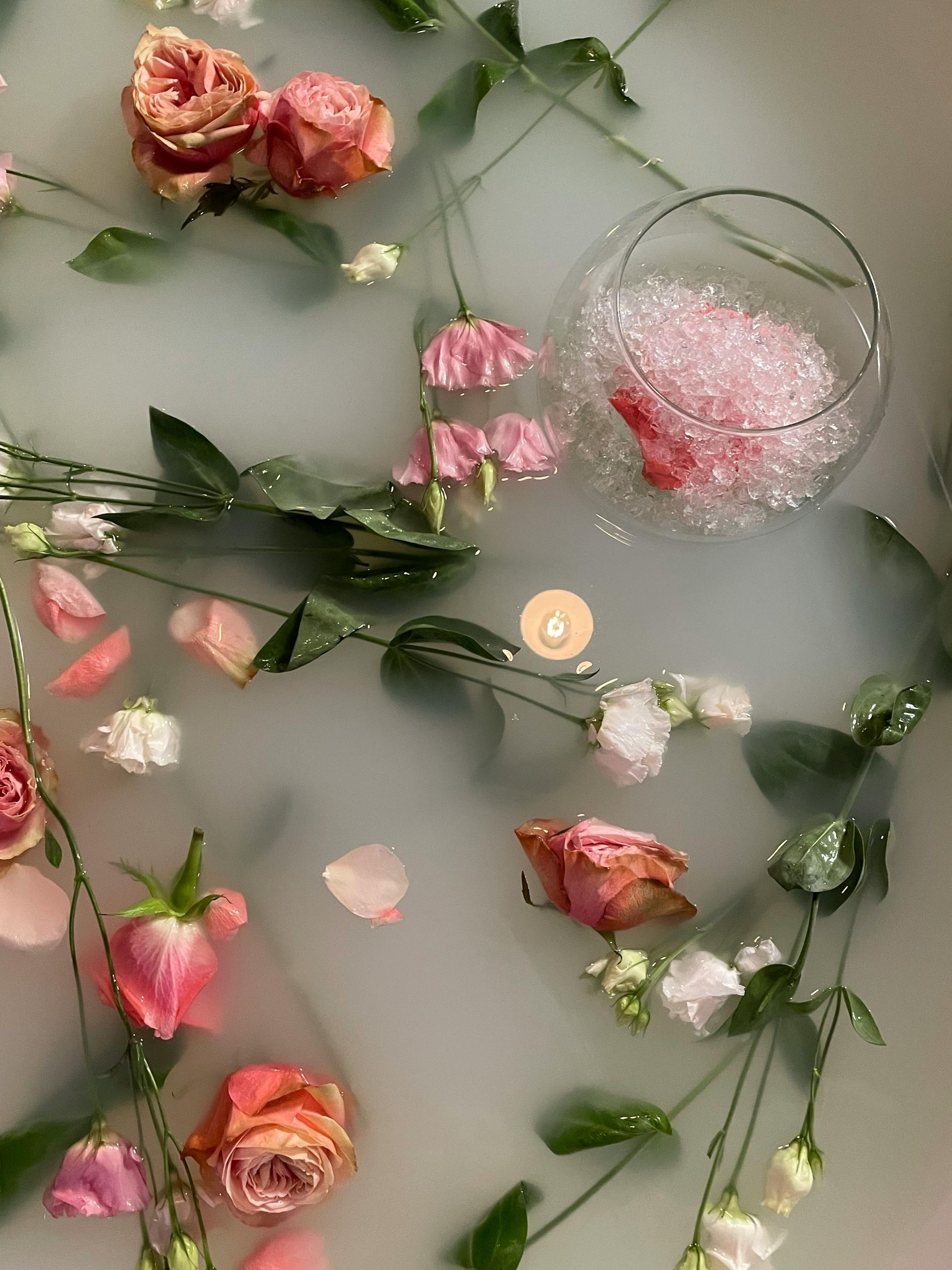 Pink roses and petals floating in cloudy water with a glass bowl of pink bubbles