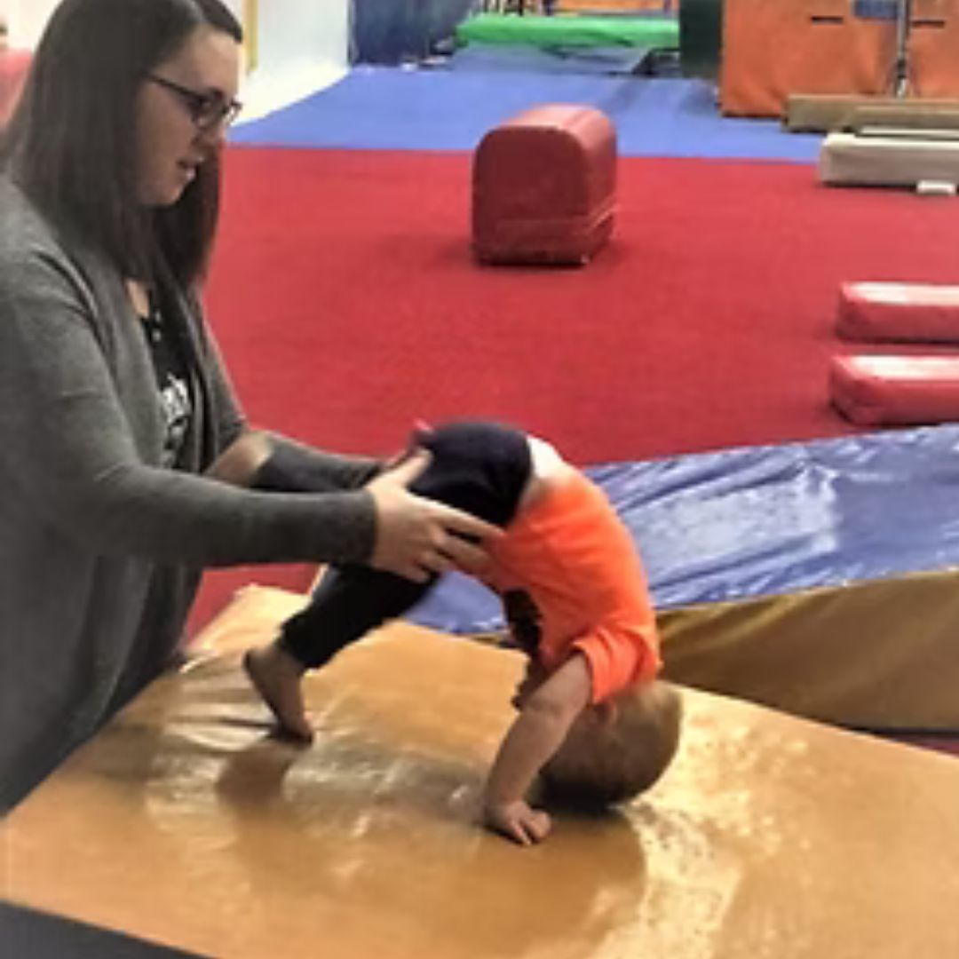A woman is helping a child do a handstand on a mat