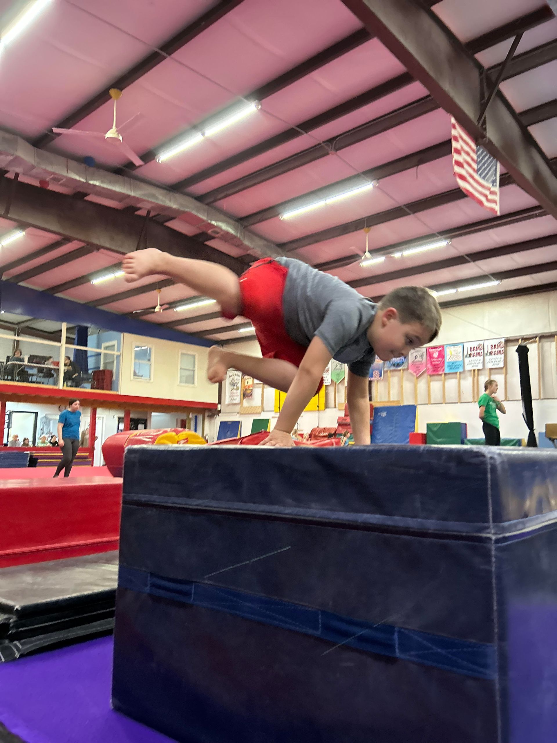 A young boy is doing a handstand on a box in a gym