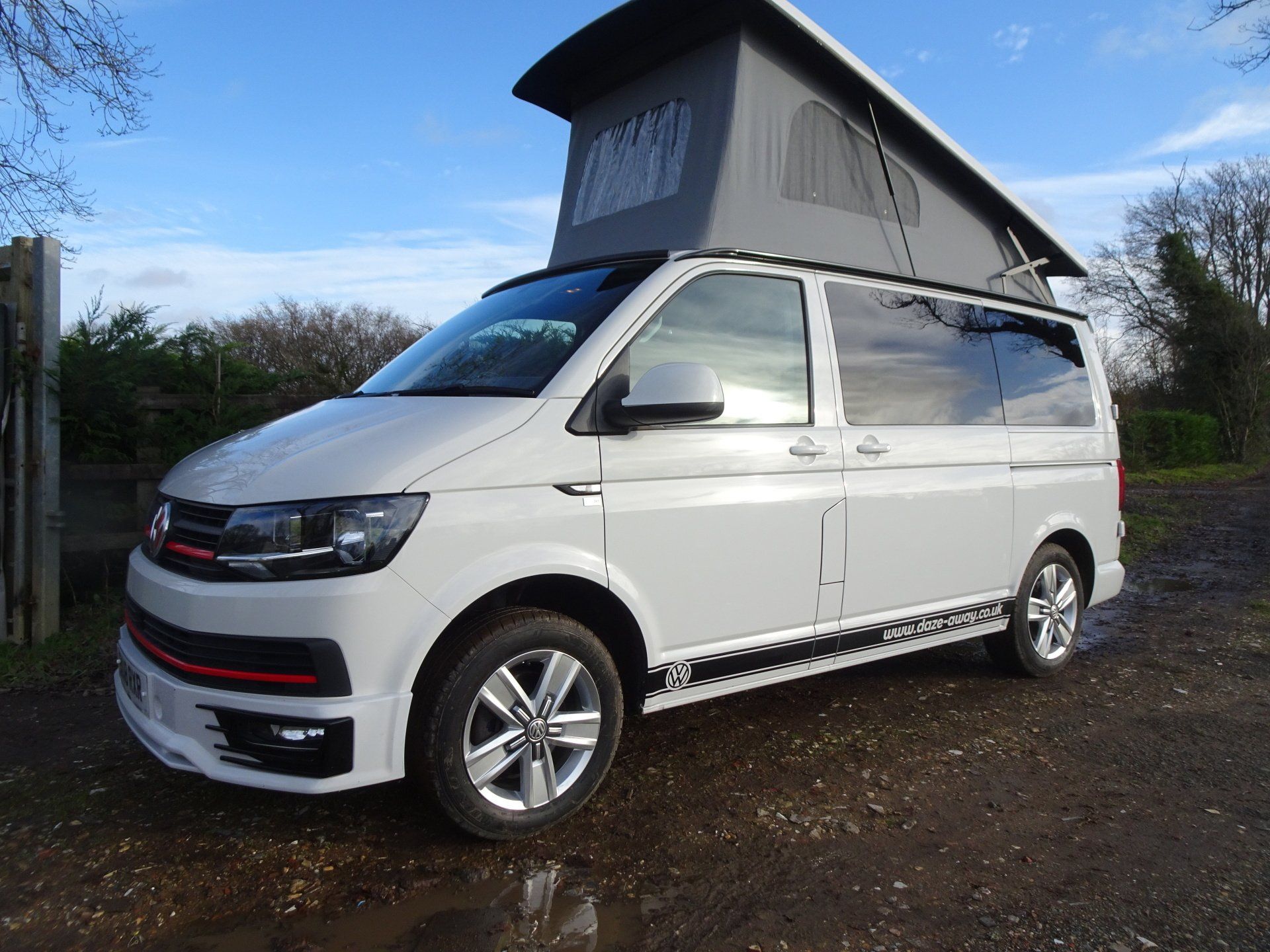 a white van with a pop top roof is parked on a dirt road .