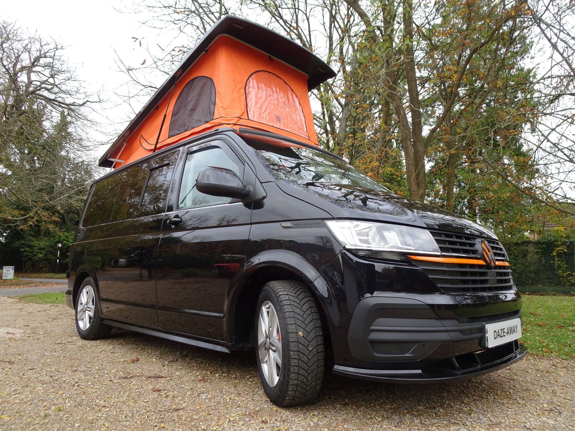 A black van with an orange roof is parked on a gravel road.