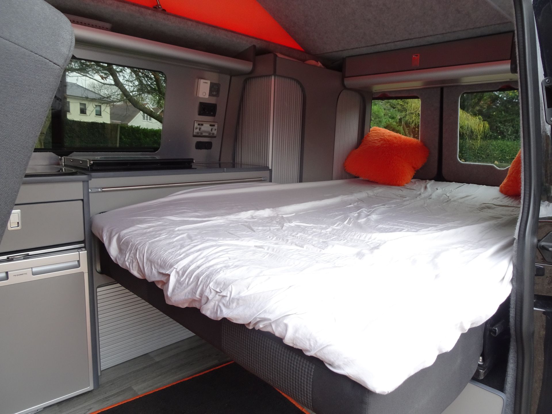 A bed in the back of a van with orange pillows