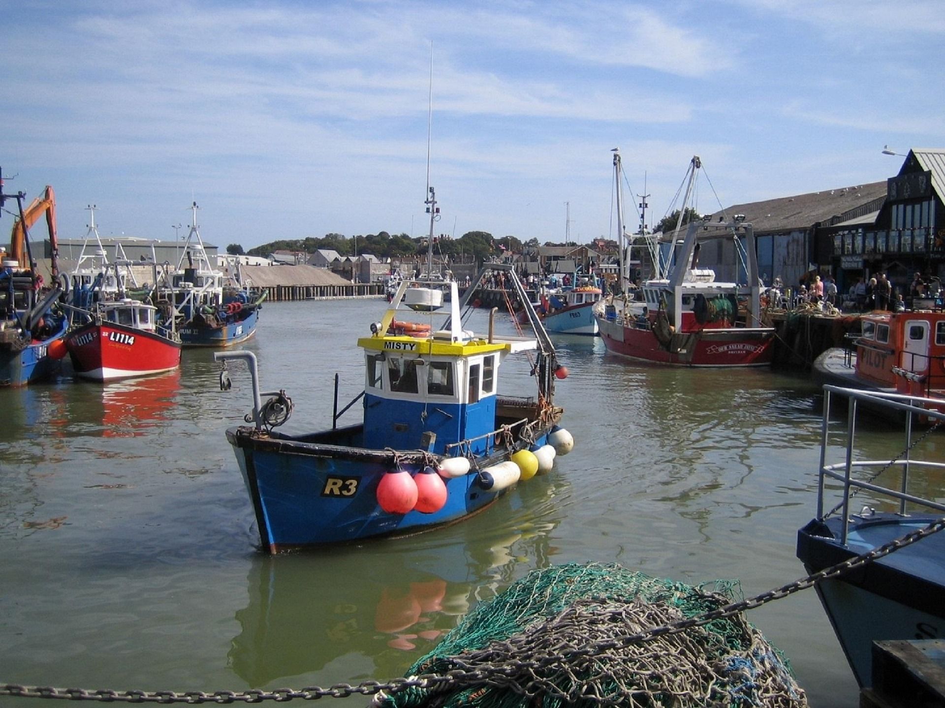 Fishing boats in Whitstable harbour, Kent, UK with colourful nets and seaside buildings