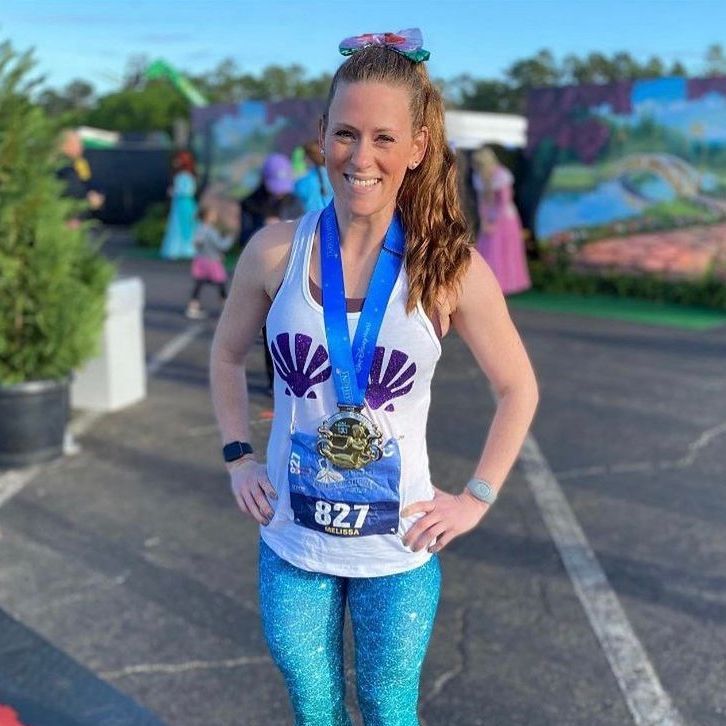 A woman wearing a mermaid tank top and leggings is standing in a parking lot with her hands on her hips.
