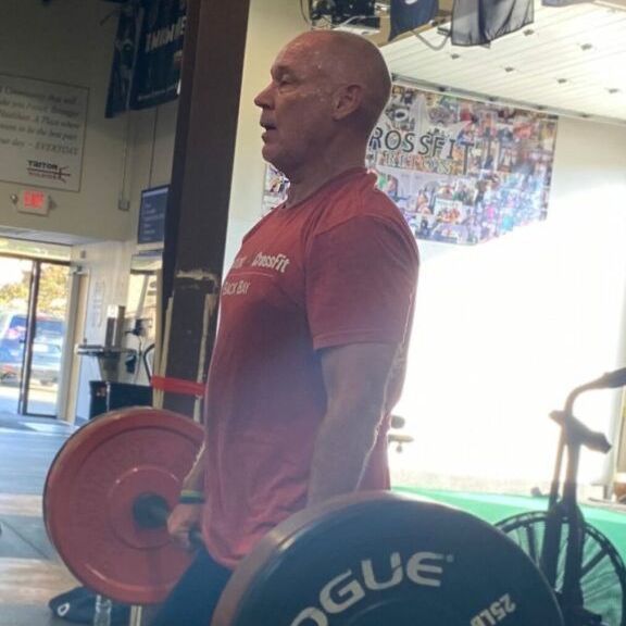 A man in a red shirt is lifting a rogue barbell