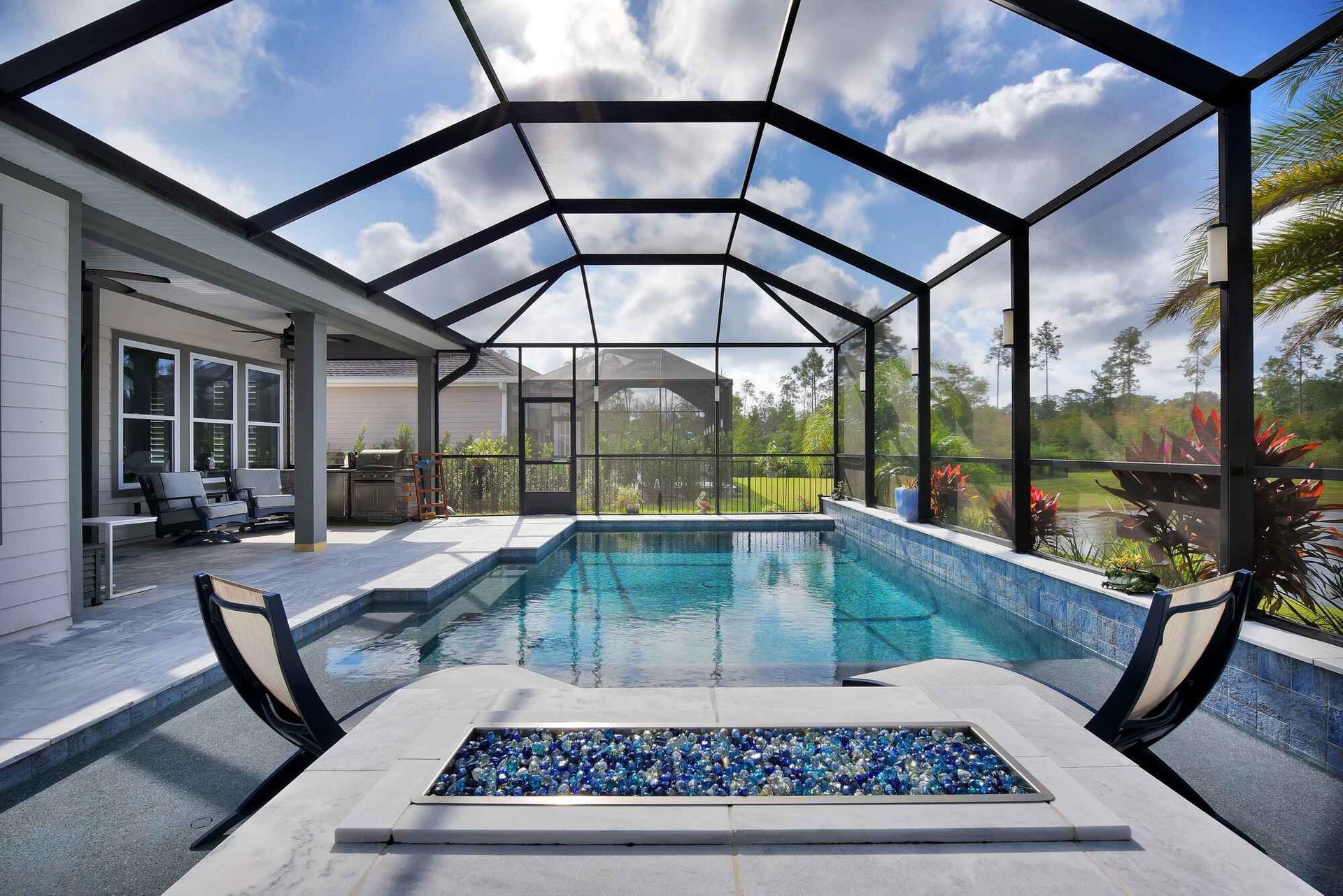 There is a swimming pool in the backyard of a house with a screened in area.