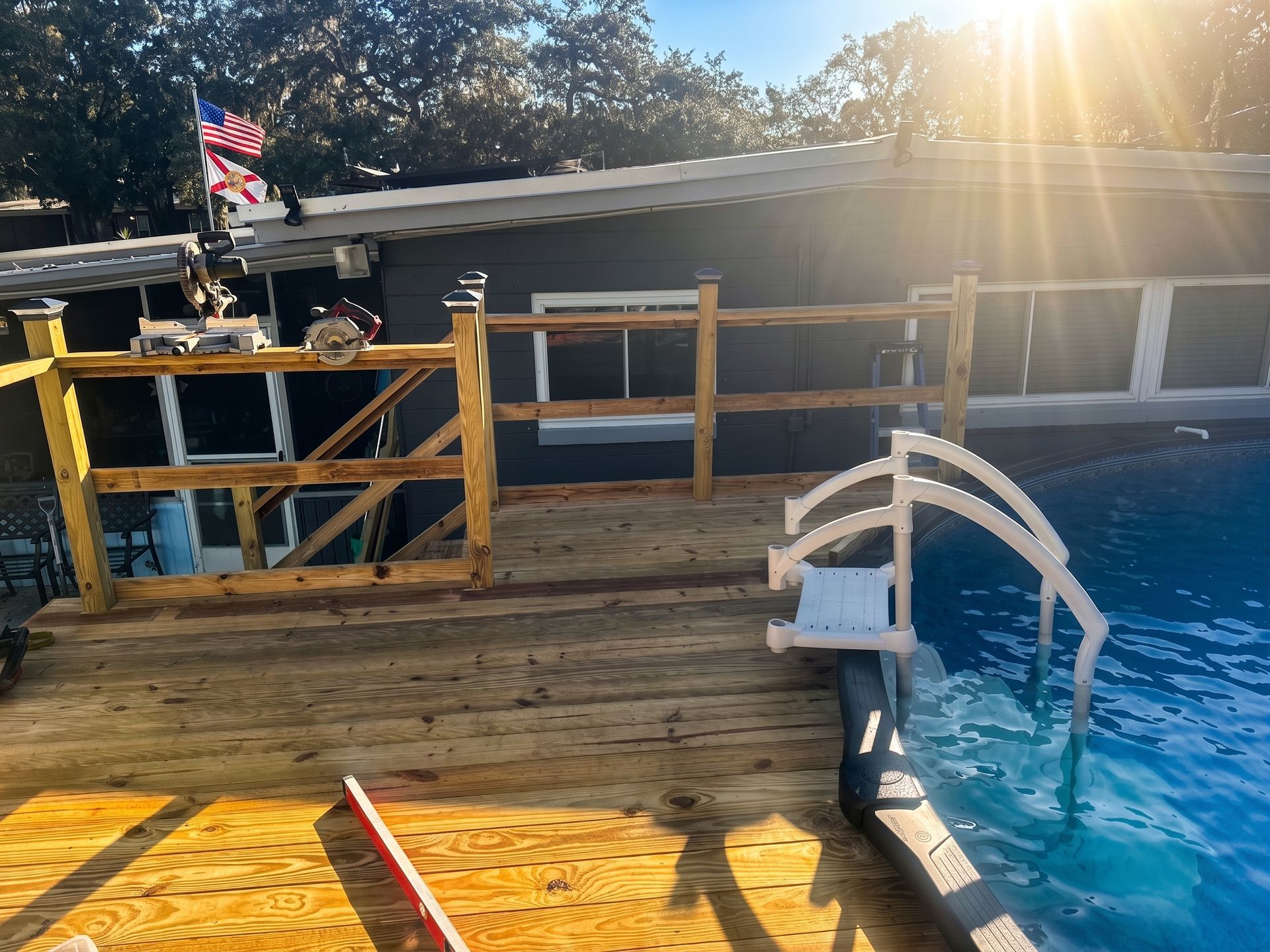 Two people sitting on the edge of an above-ground pool in a backyard patio area