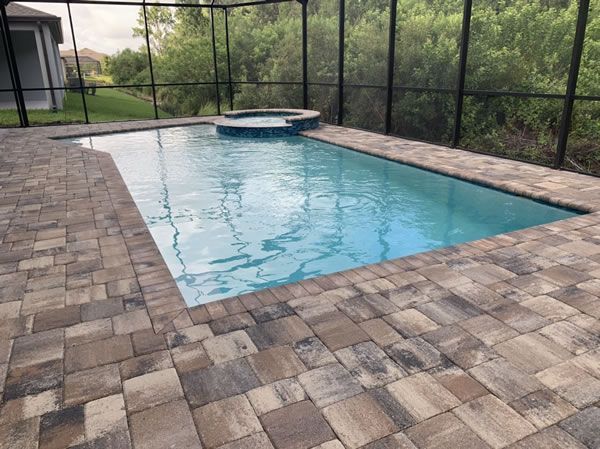 Pool and hot tub with brick pavers surrounded by a screened enclosure; water is light blue.