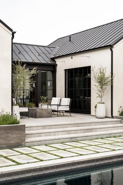 Outdoor patio with seating, fireplace, and potted plants, adjacent to a pool and modern house.