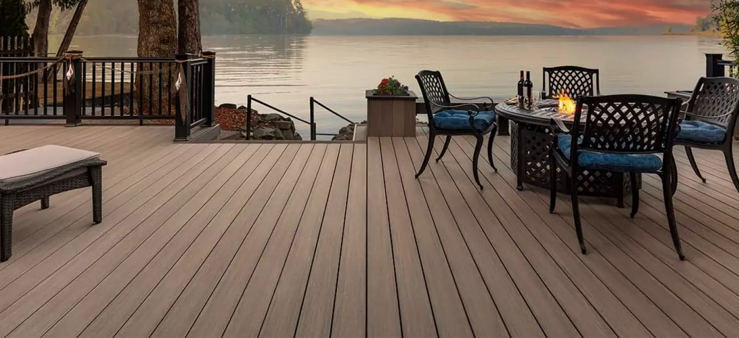 Composite deck with patio chairs and table overlooking a calm lake at sunset