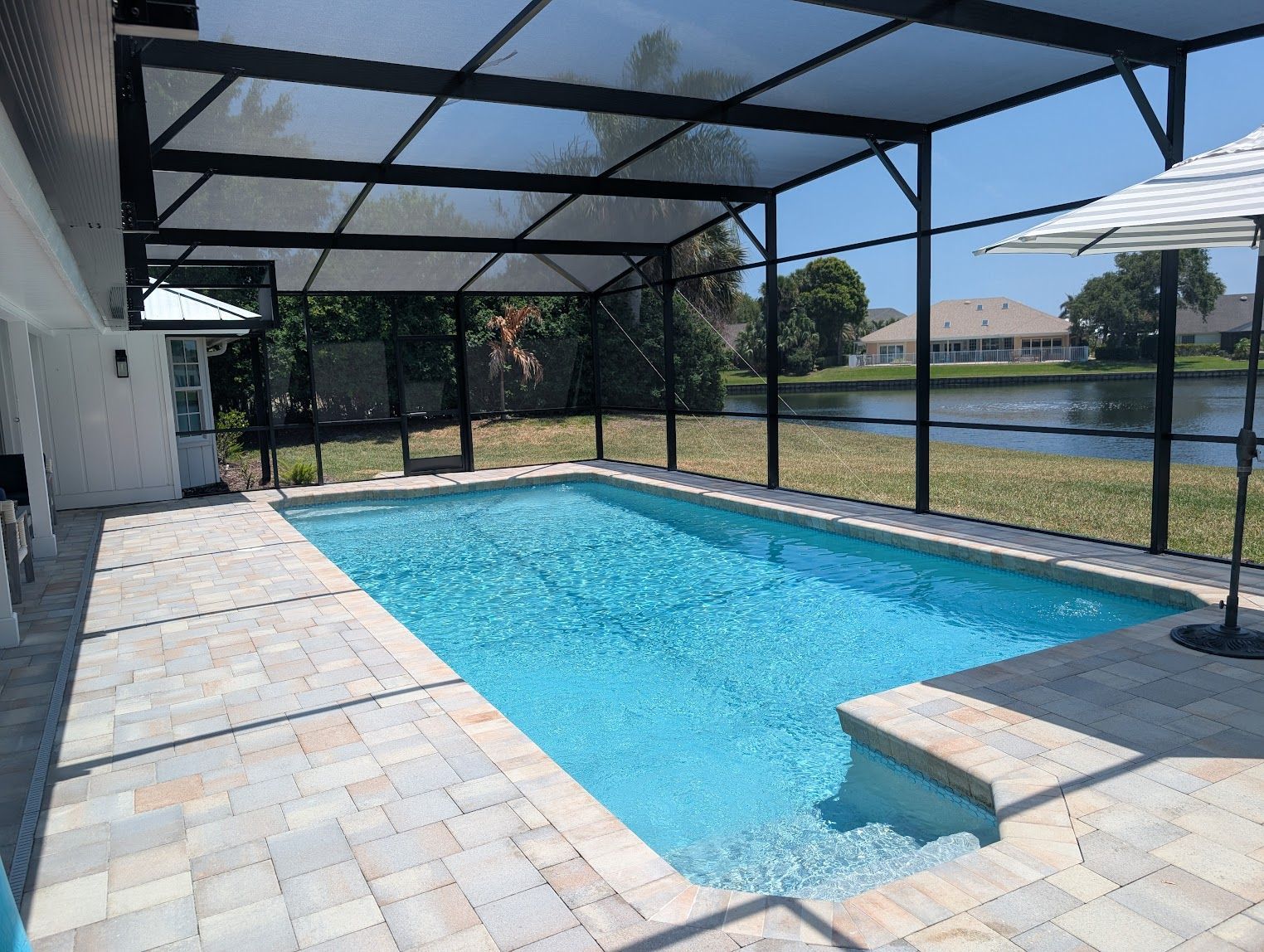 There is a swimming pool in the backyard of a house with a screened in area.
